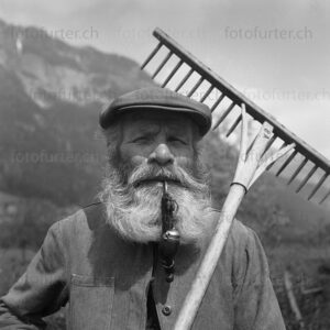Porträt von altem Bauern mit Bart, Pfeife und Rechen, fotografiert von Otto Furter